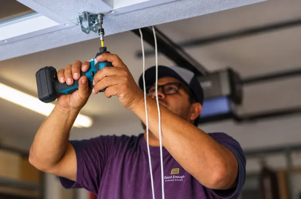 Good Enough Garage Doors technician in the plum uniform fastening a garage door opener bracket with a drill